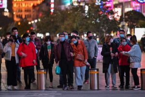 People wearing face masks amid concerns over the COVID-19 coronavirus outbreak walk along a shopping district in Shanghai on March 20, 2020. (Photo by Hector RETAMAL / AFP)